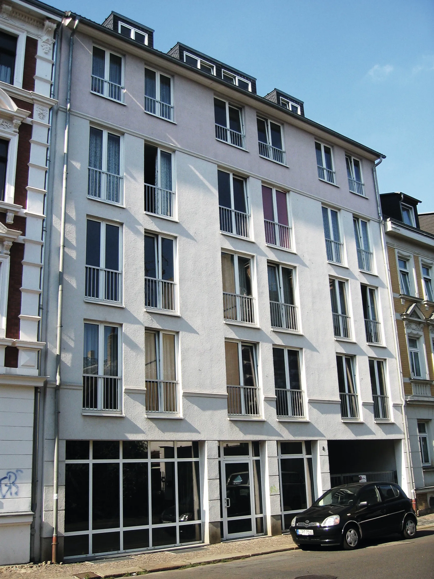 Hellgrauer Neubau mit hohen Fenstern und Ladenfläche im Erdgeschoss